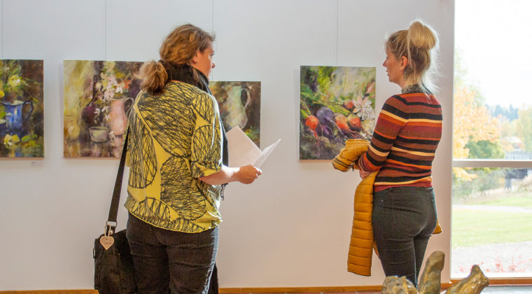 Kaksi ihmistä katselemassa värikkäitä taideteoksia Kuusankoskitalon galleriassa.